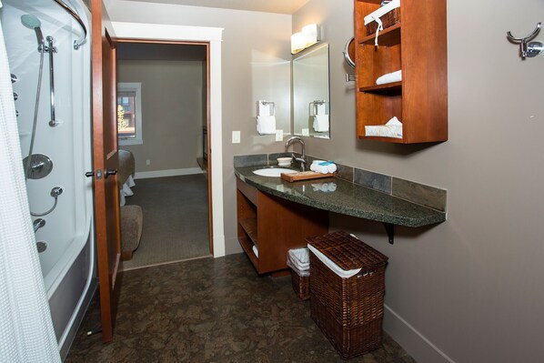 Une salle de bain avec une douche, un lavabo et un miroir. On y trouve un panier en osier et un porte-serviettes.