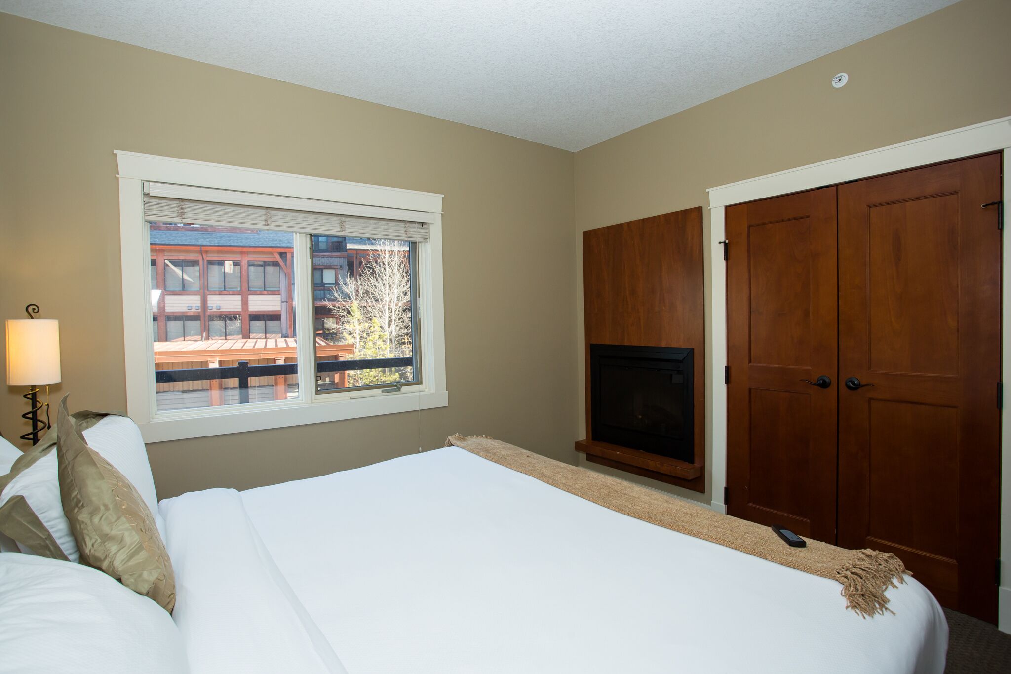 Un dormitorio con cama, televisión, ventana con vista a un edificio y armarios de madera.