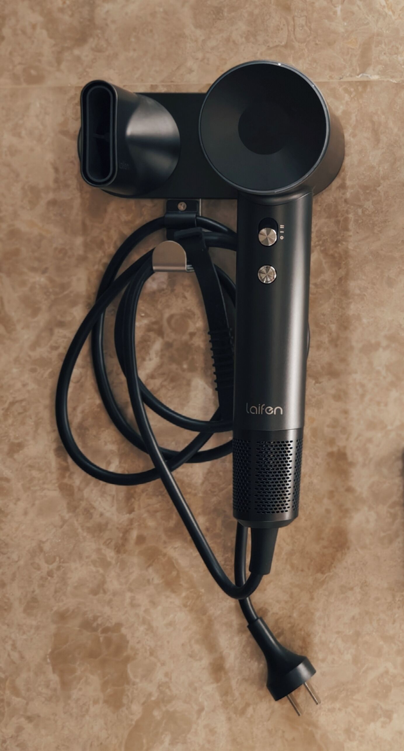 A black hairdryer with a cord and a plug, placed on a textured surface.