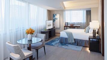 A modern hotel room with a bed, a desk, a chair, a TV, and a window with curtains.