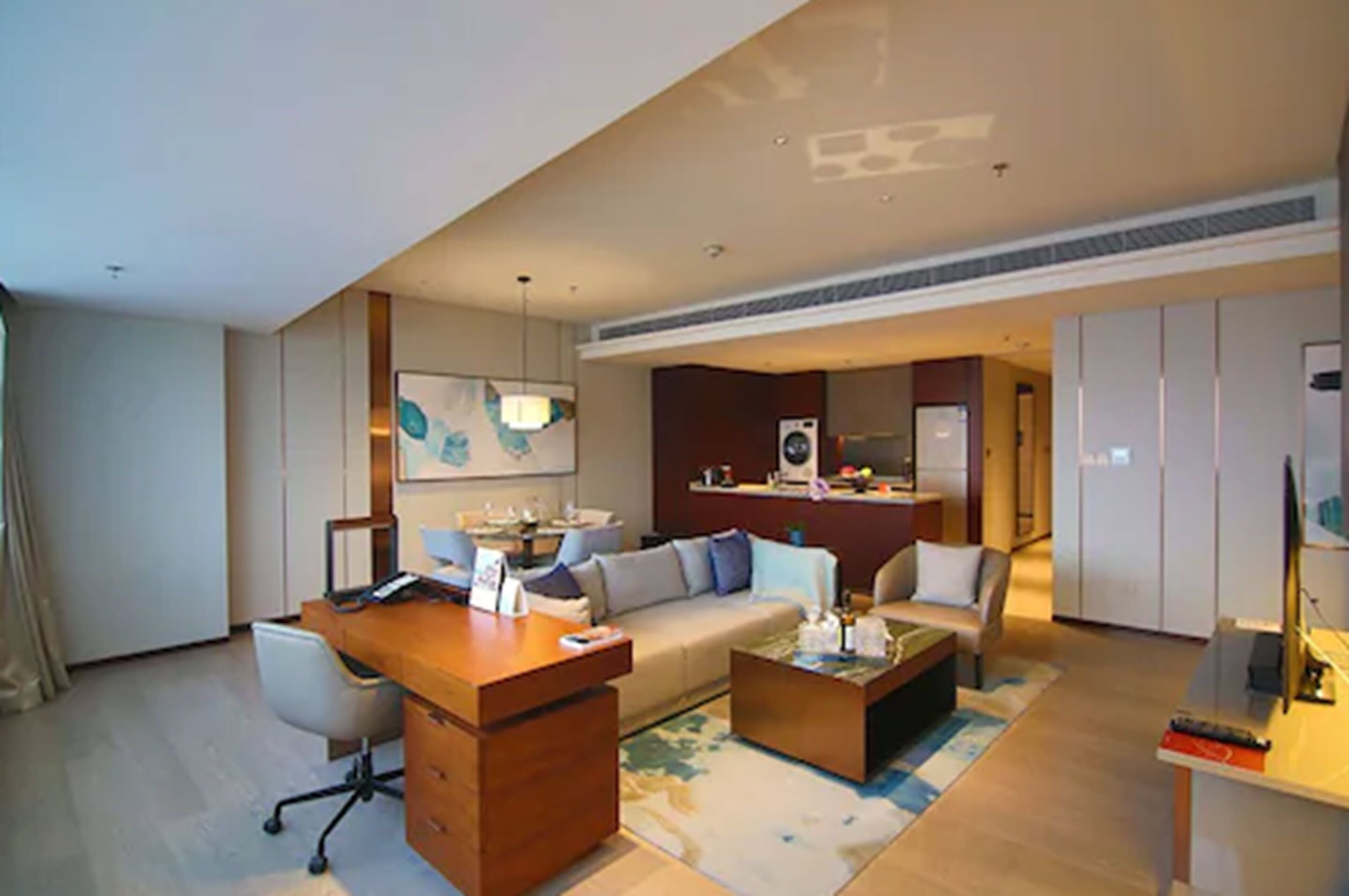 A modern hotel room with a wooden desk, a sofa, a coffee table, and a television.