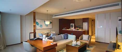 A modern hotel room with a wooden desk, a sofa, a coffee table, and a television.