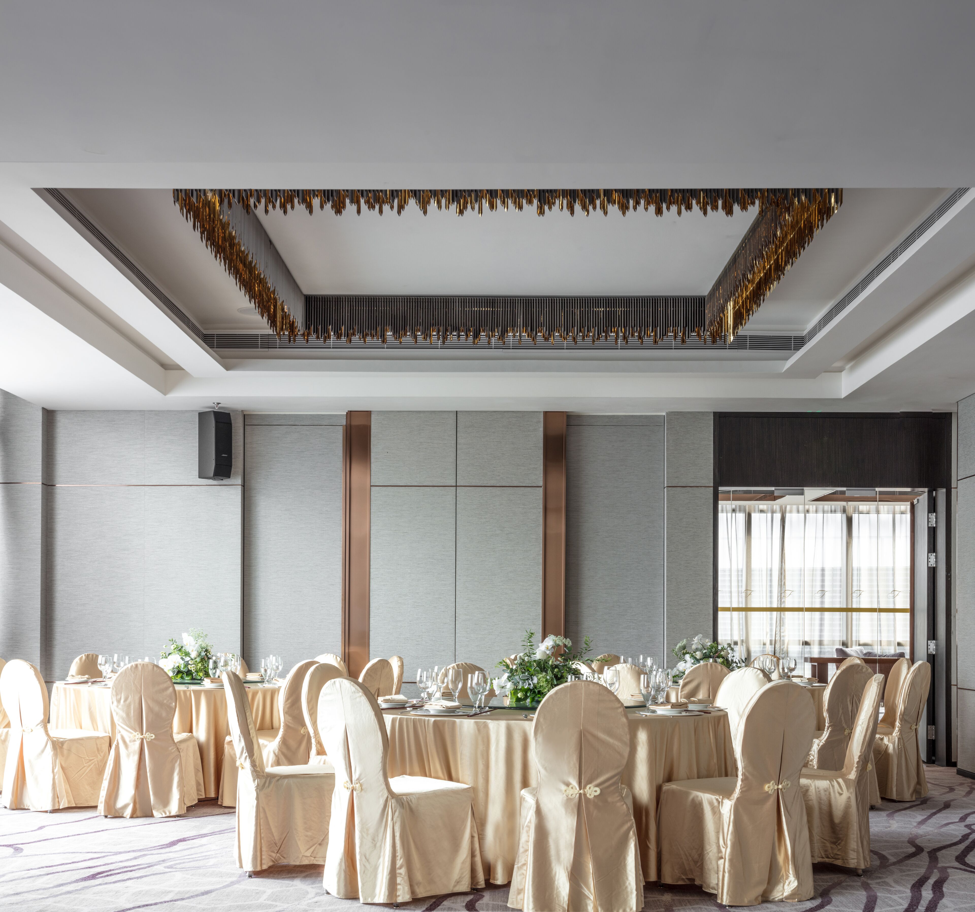 Un salón de banquetes con mesas redondas, sillas color beige y un techo decorativo.