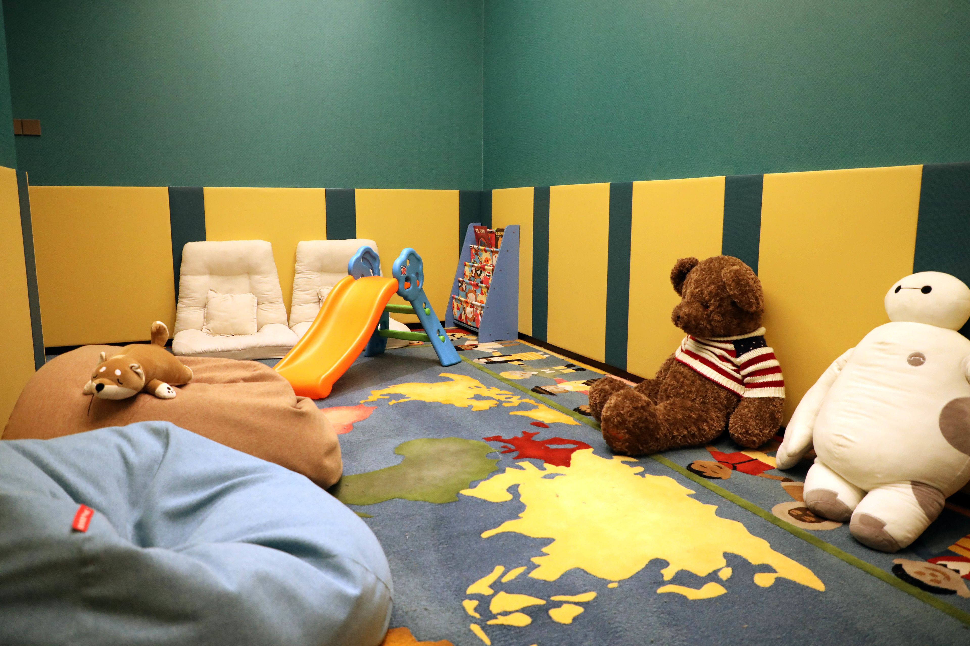 A children's playroom with a soft play area, a bookshelf, and plush toys.