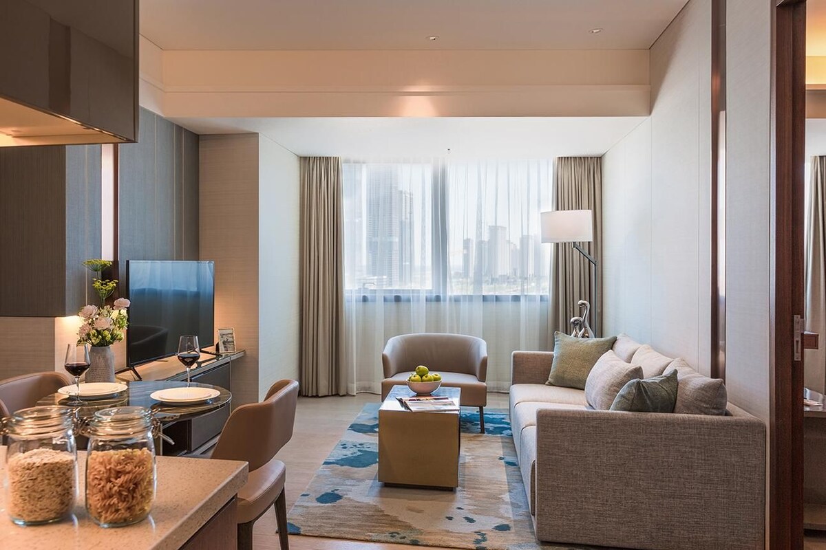 Habitación de hotel moderna con comedor, sofá, televisión y vistas a la ciudad.
