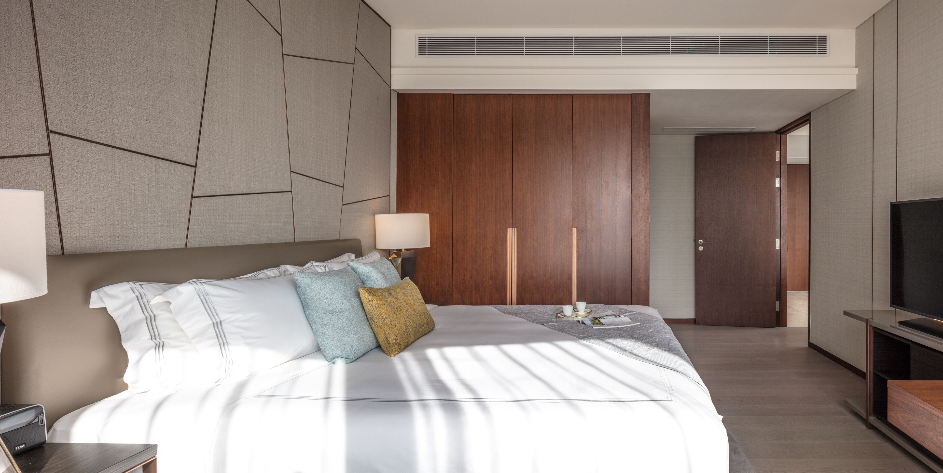A modern hotel room with a large bed, a TV, and a wooden wardrobe.