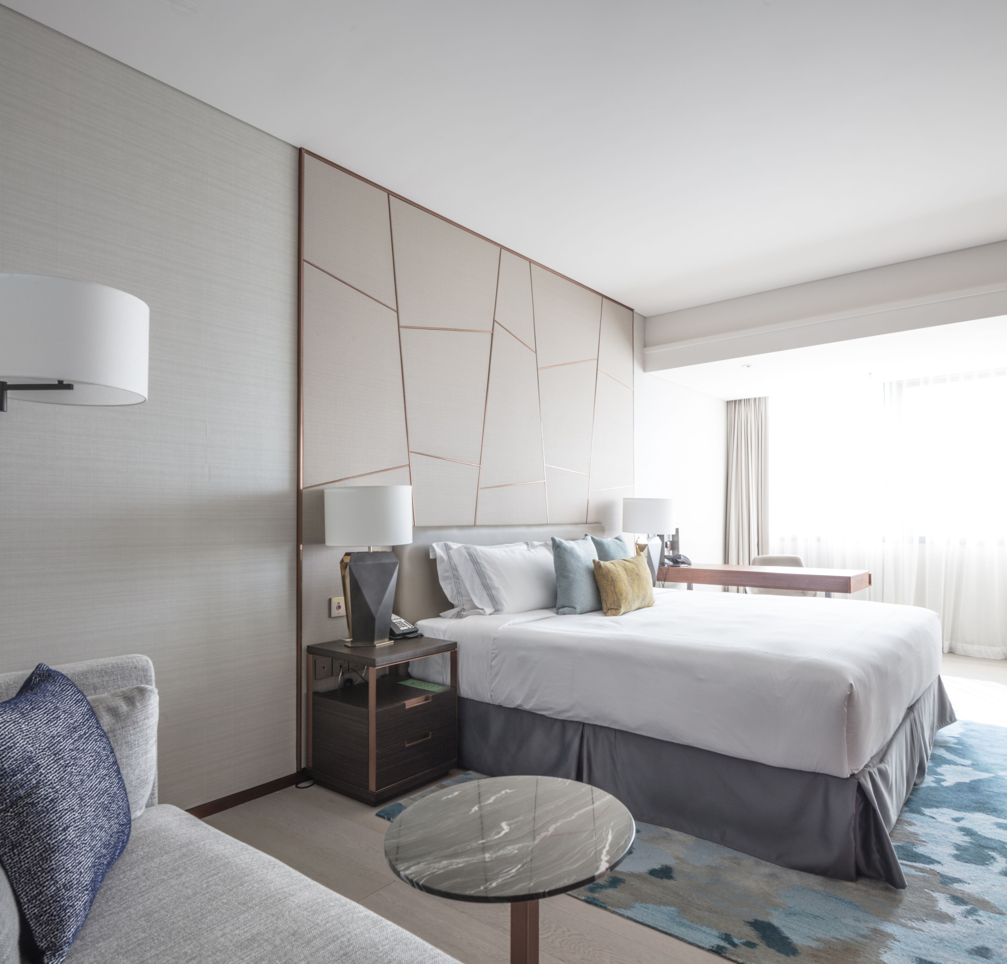 Ein modernes Hotelzimmer mit einem großen Bett, einem Nachttisch mit Lampe, einem kleinen runden Tisch und einer Couch.