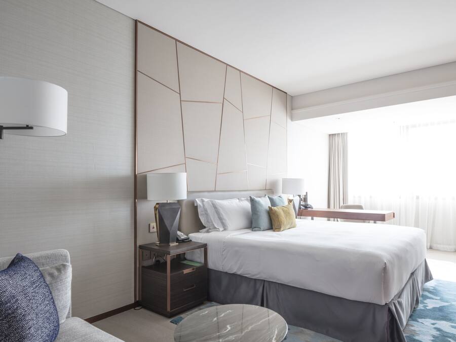 Ein modernes Hotelzimmer mit einem großen Bett, einem Nachttisch mit Lampe, einem kleinen runden Tisch und einer Couch.