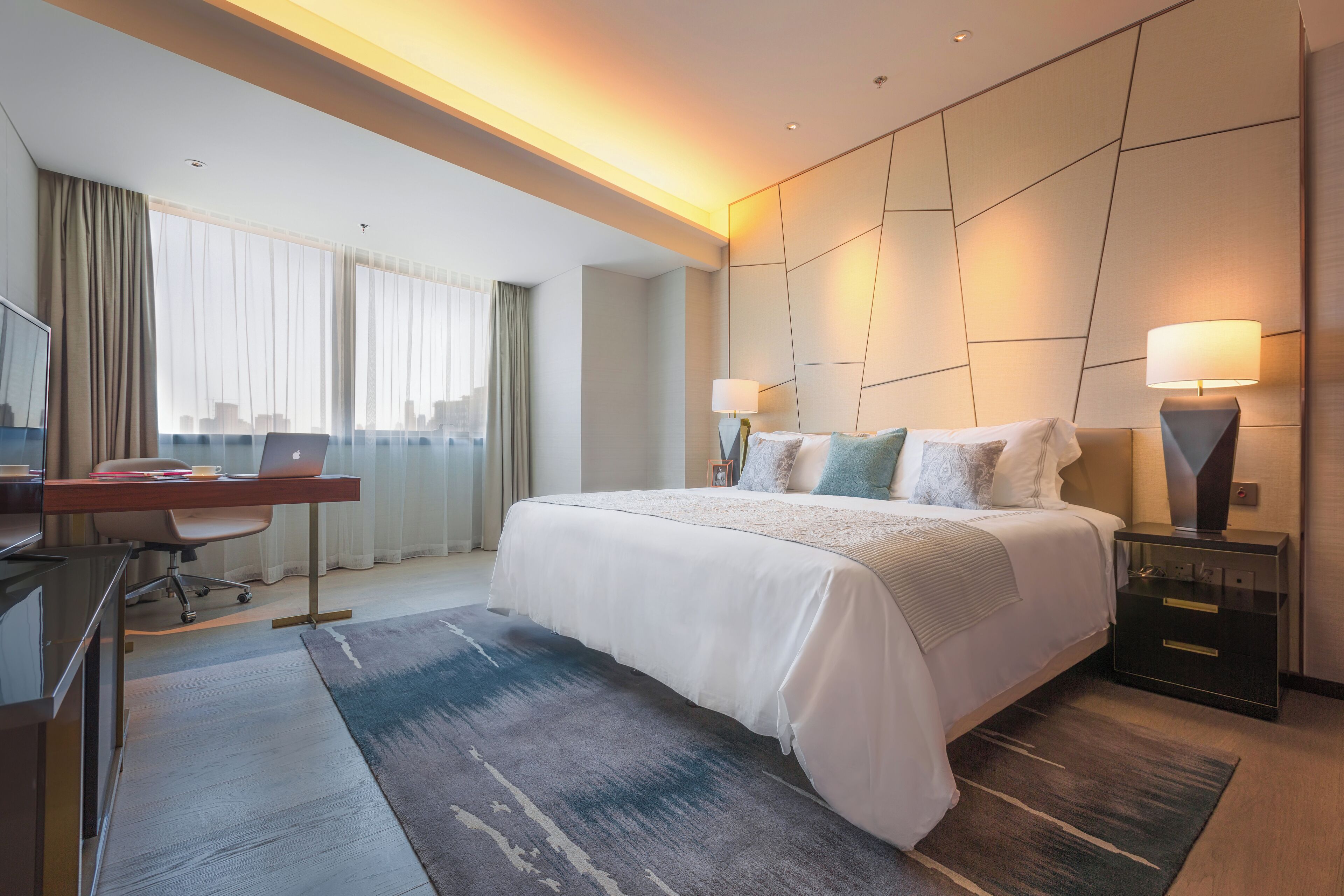 Ett modernt hotellrum med en stor säng, ett skrivbord med en bärbar dator och utsikt över staden genom fönstret.