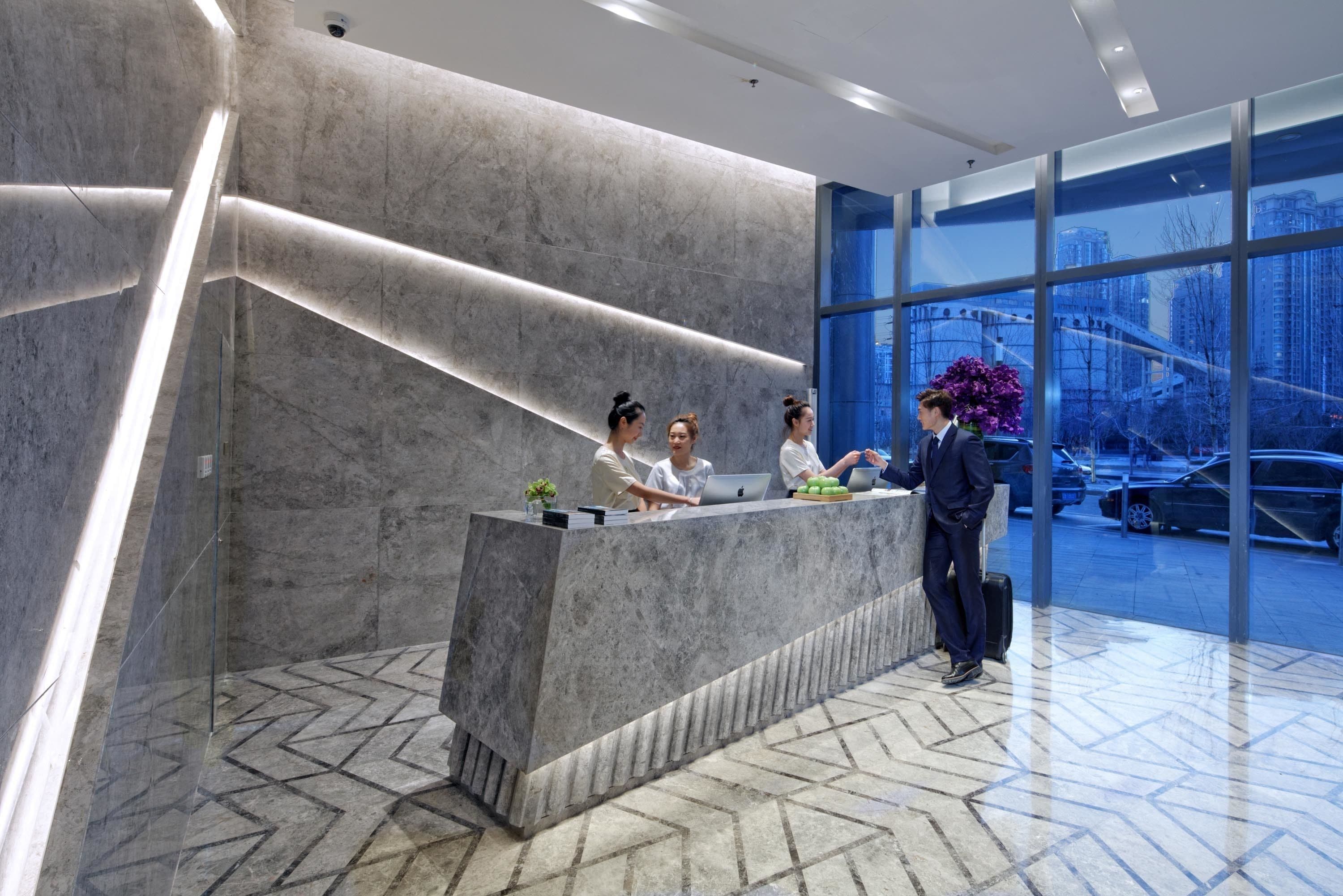 A reception desk with three staff members, a large window with a view of buildings and cars, and a modern interior design.