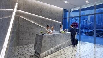 A reception desk with three staff members, a large window with a view of buildings and cars, and a modern interior design.