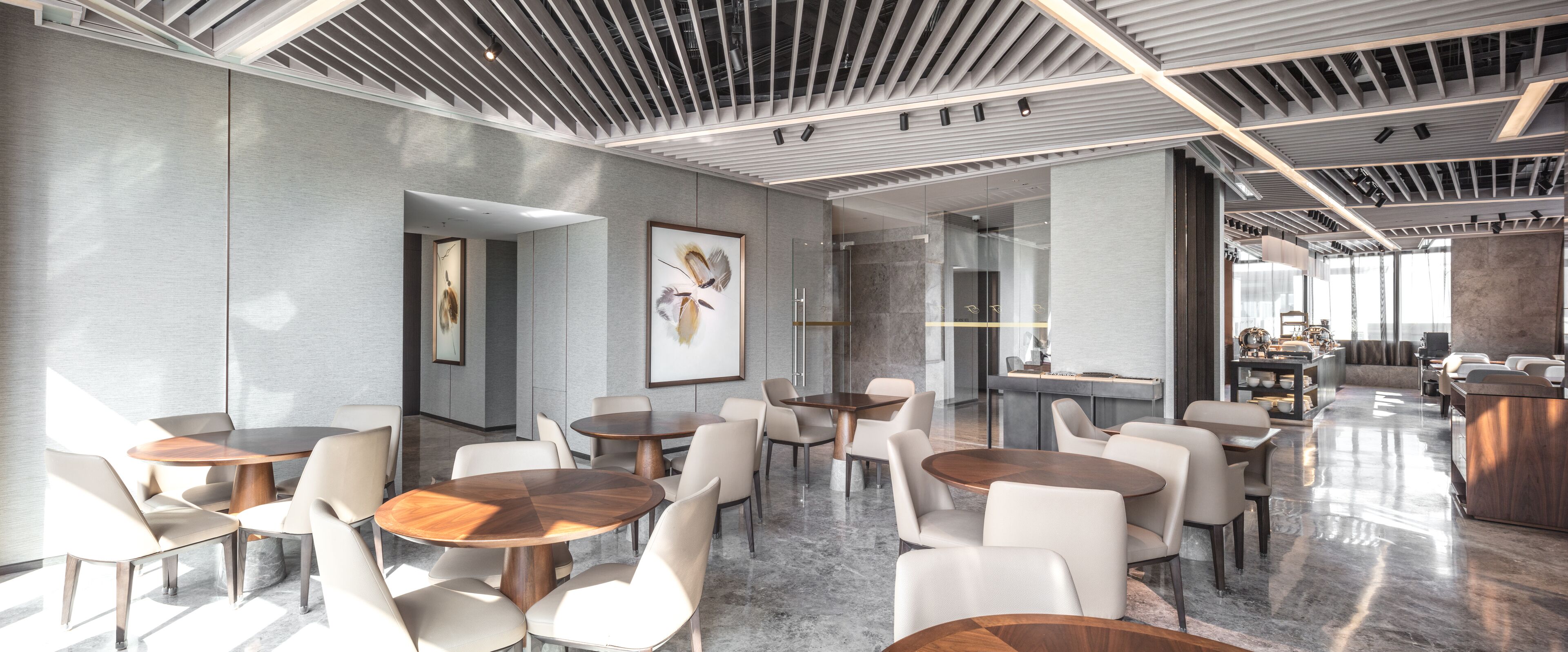 Een moderne hotellobby met ronde tafels en stoelen, een receptiebalie en een groot raam dat natuurlijk licht binnenlaat.