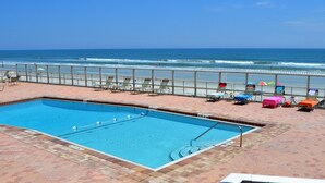 Zona de piscina con vistas al océano, sillas de descanso y sombrillas.