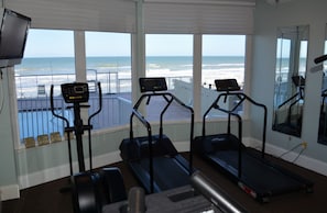 A gym with treadmills and a TV, overlooking a beach.