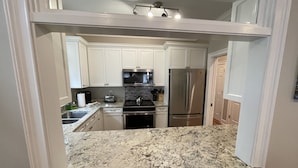 A kitchen with white cabinets, a stainless steel refrigerator, a microwave, and a granite countertop. - Ocean Views, Steps to the Beach & GP Pools, Monthly Long Term discounts (Isle of Palms)