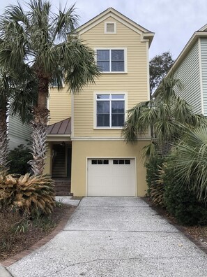 A two-story house with a garage, surrounded by palm trees and other vegetation. - Ocean Views, Steps to the Beach & GP Pools, Monthly Long Term discounts (Isle of Palms)