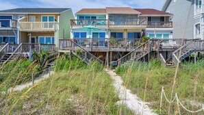 Una proprietà fronte spiaggia con edifici a più piani, terrazze all'aperto e un sentiero sabbioso che conduce alla spiaggia.