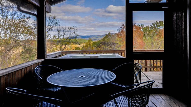 Una terraza de madera con mesa y sillas, con vistas a un paisaje pintoresco de árboles y colinas.