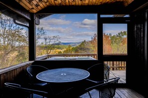 Una terraza de madera con mesa y sillas, con vistas a un paisaje pintoresco de árboles y colinas.
