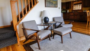 Una sala de estar con una escalera, dos sillones, una mesita con una lámpara y un cuadro en la pared.