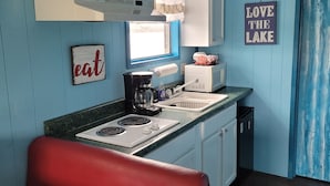Una cocina compacta con estufa, lavamanos y un banco rojo. Hay armarios sobre la encimera y un letrero que dice "Love the Lake".