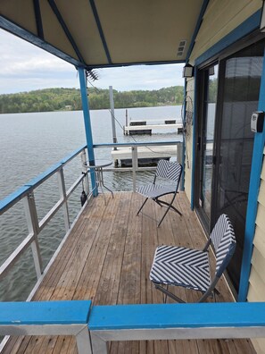 A covered deck with two chairs, a table, and a view of a dock and water. - Floating Cabin Lake Guntersville Cabin number 118 (Guntersville)