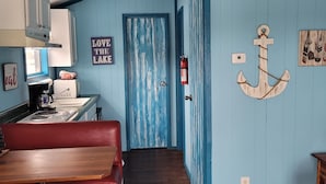 Un pasillo estrecho con suelo de madera, una puerta azul y un adorno de ancla en la pared.