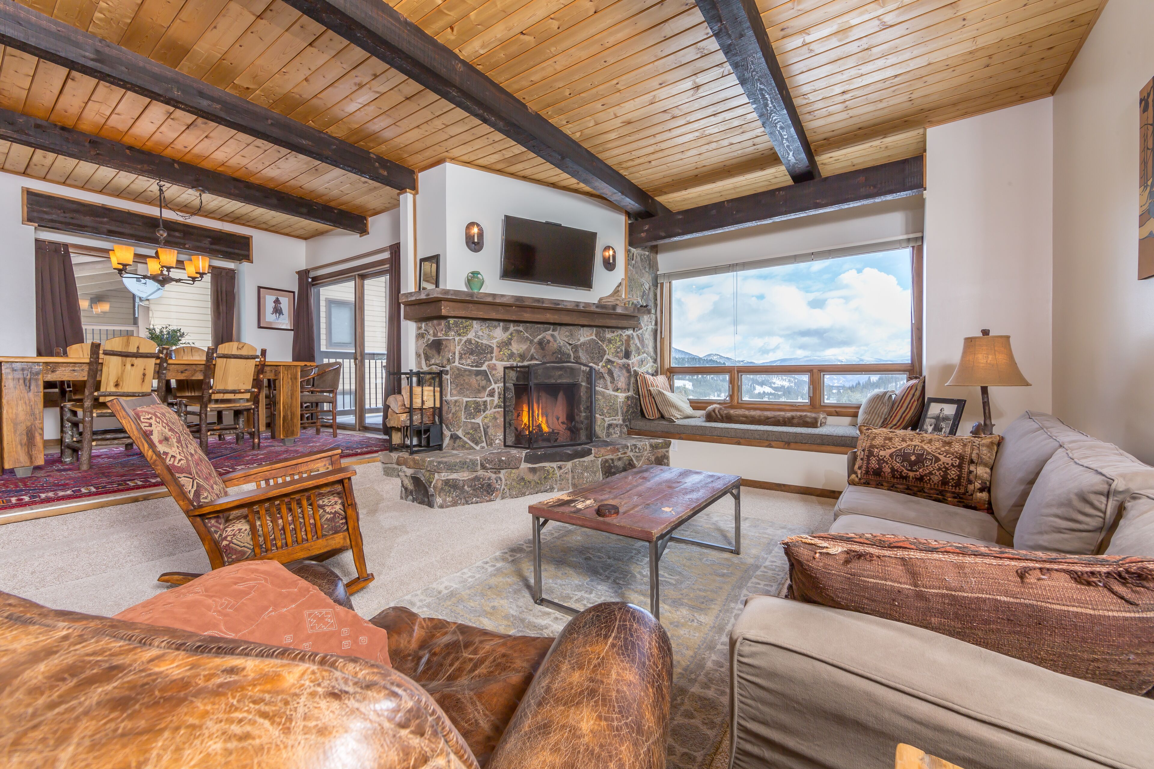 Una sala de estar acogedora con chimenea de piedra, mobiliario de madera y un ventanal con vistas panorámicas.