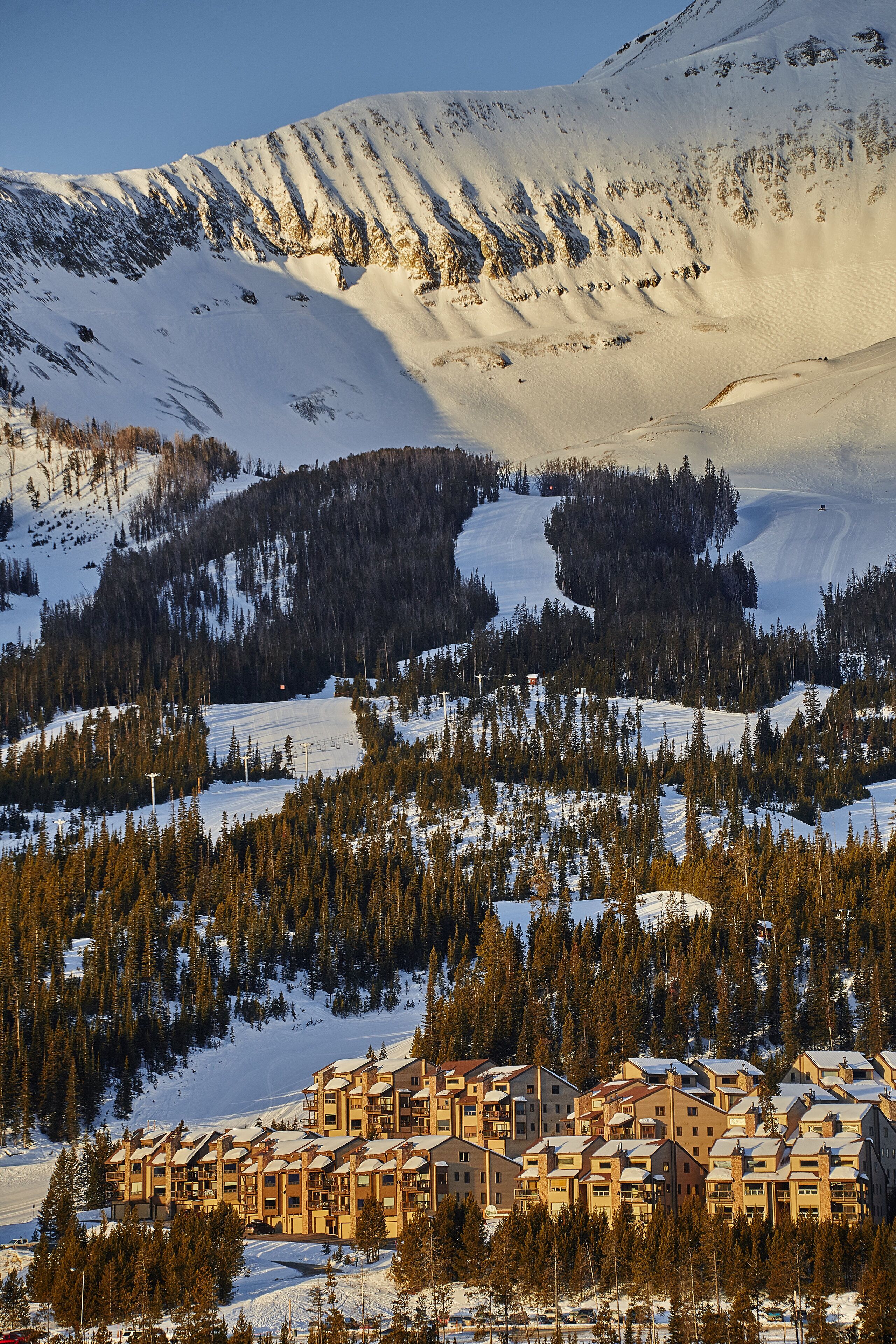A mountain lodge with multiple buildings, surrounded by snow-covered terrain and dense forests.