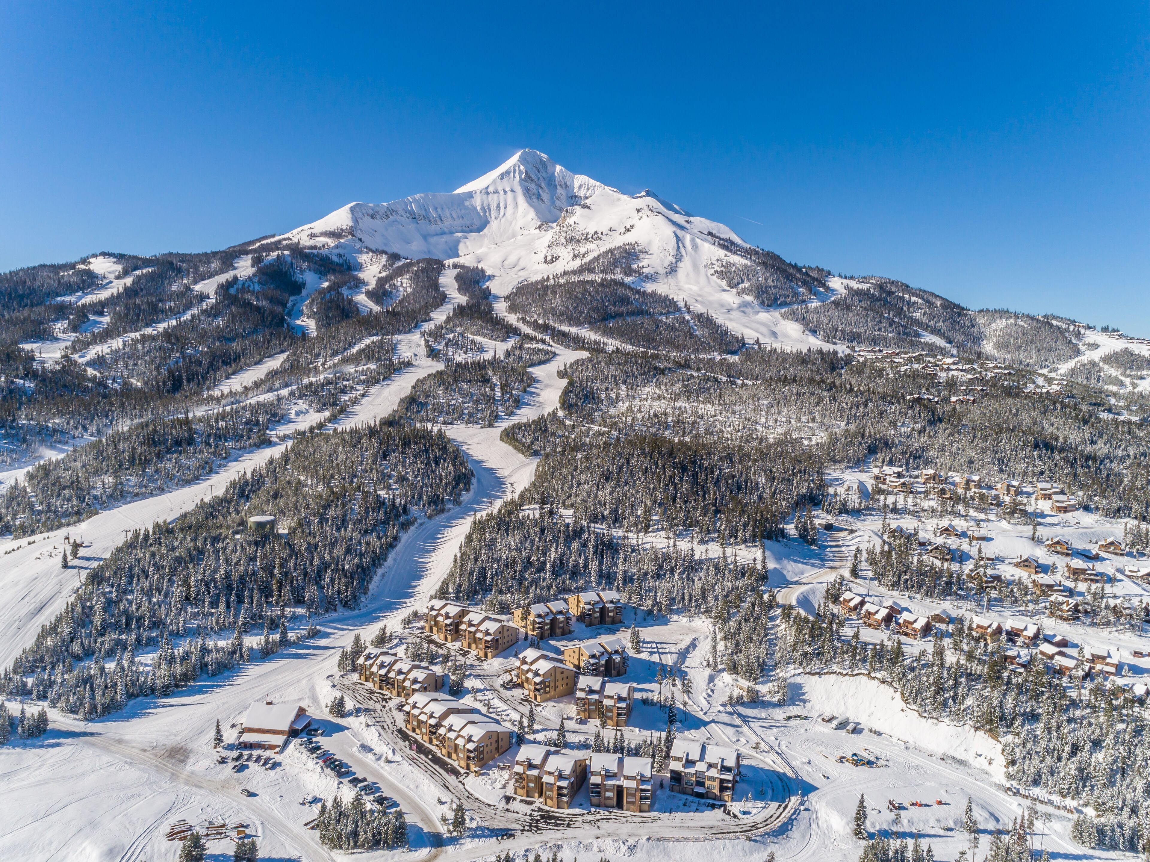 A snow-covered mountain with a ski resort at its base, featuring multiple chalet-style buildings and ski trails.