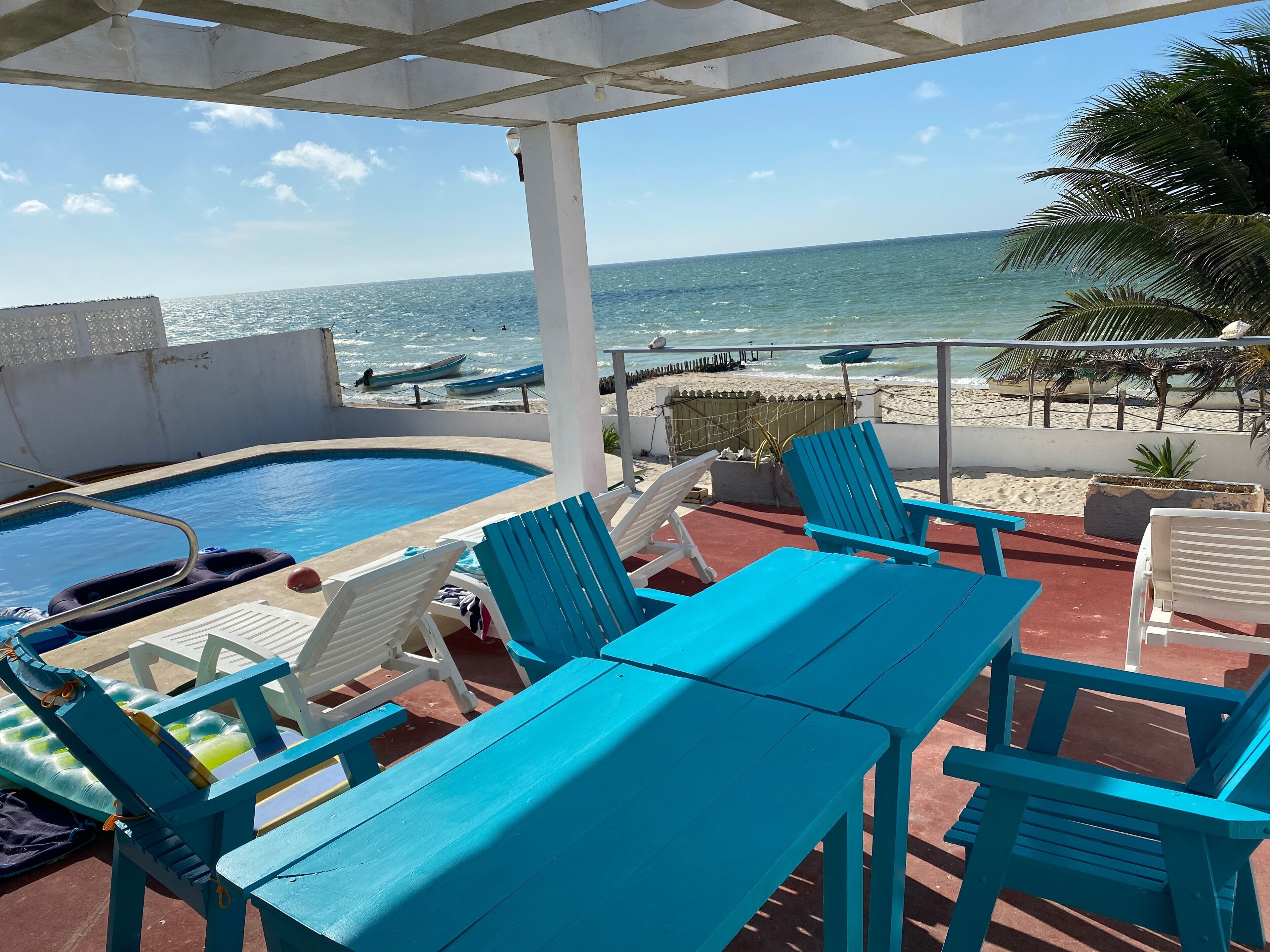 A pool area with blue chairs and a table, overlooking the beach and ocean.