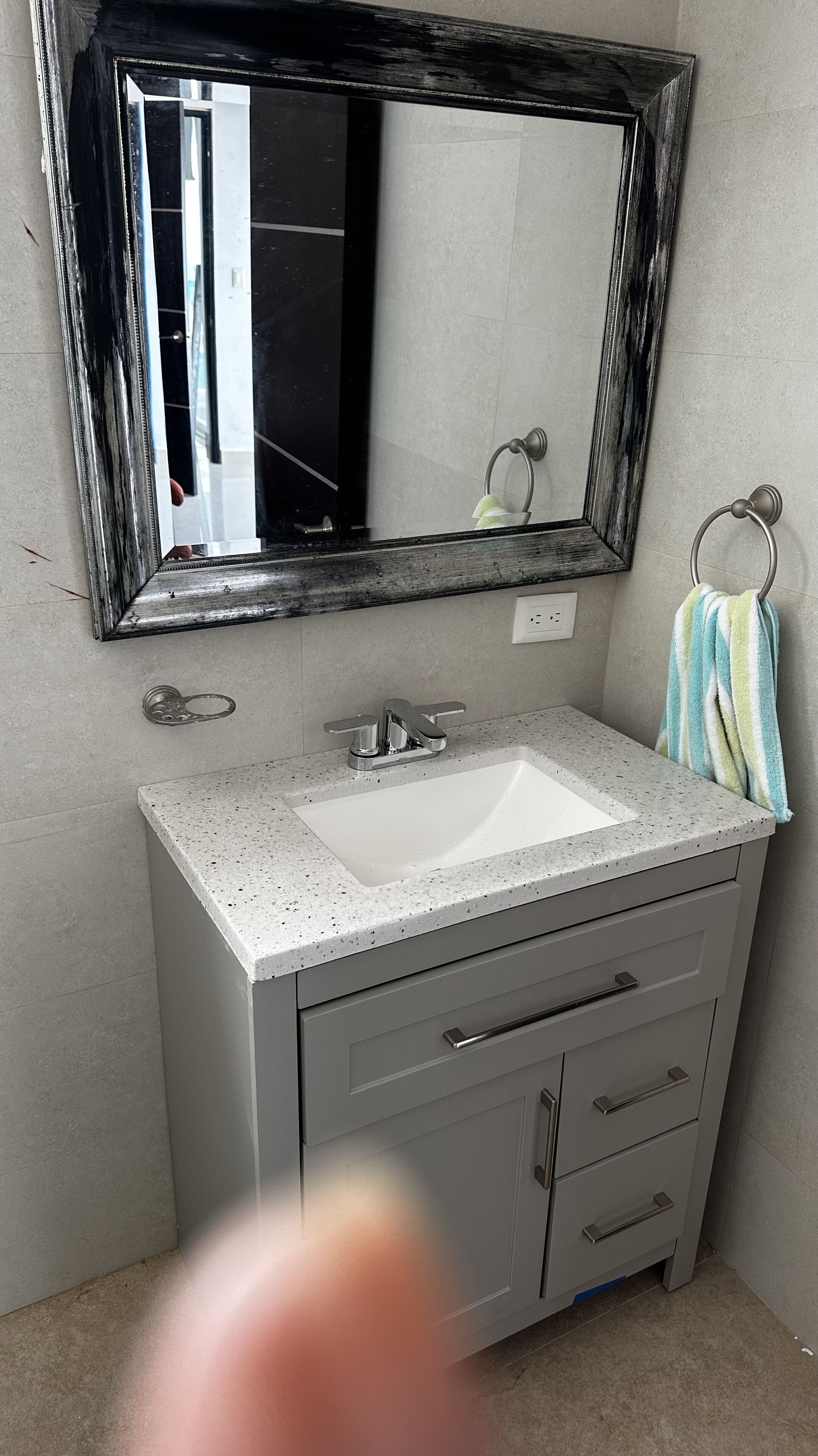 Uma casa de banho com uma pia branca, um espelho com moldura escura, um porta-toalhas e uma toalha listrada, e uma torneira.