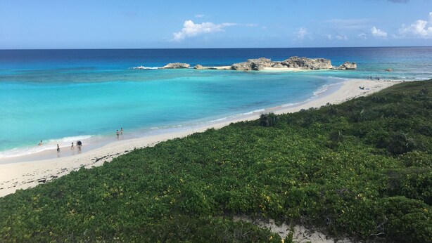 A beach with clear turquoise water, a sandy shore, and rocky outcrops in the distance.