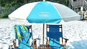 A beach chair and umbrella setup with a table, a bag, and flip-flops on the sand. - Gated Waters Edge, deeded beach, chair set up, private pool, 5 bed\5+ sleeps 16 (Rosemary Beach)