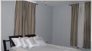 A neatly made bed with white linens and multiple pillows, a bedside table, and curtains on the windows. - Beautiful New Orleans Gem Close To Downtown (New Orleans)
