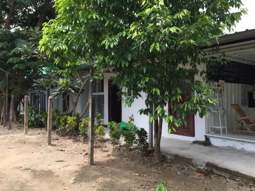 Um edifício com fachada branca, um pequeno alpendre com uma cadeira e uma árvore à frente.