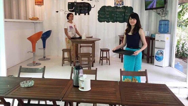 A restaurant with wooden tables and chairs, a chalkboard menu, and a television screen.