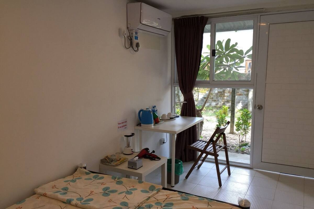 A small room with a bed, a desk, a chair, a window with curtains, and a view of greenery outside.