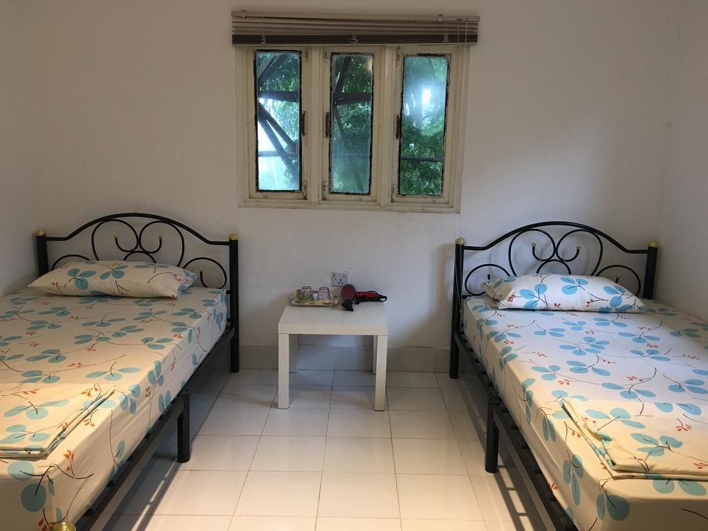 A room with two single beds, a small table, and a window with a view of trees.
