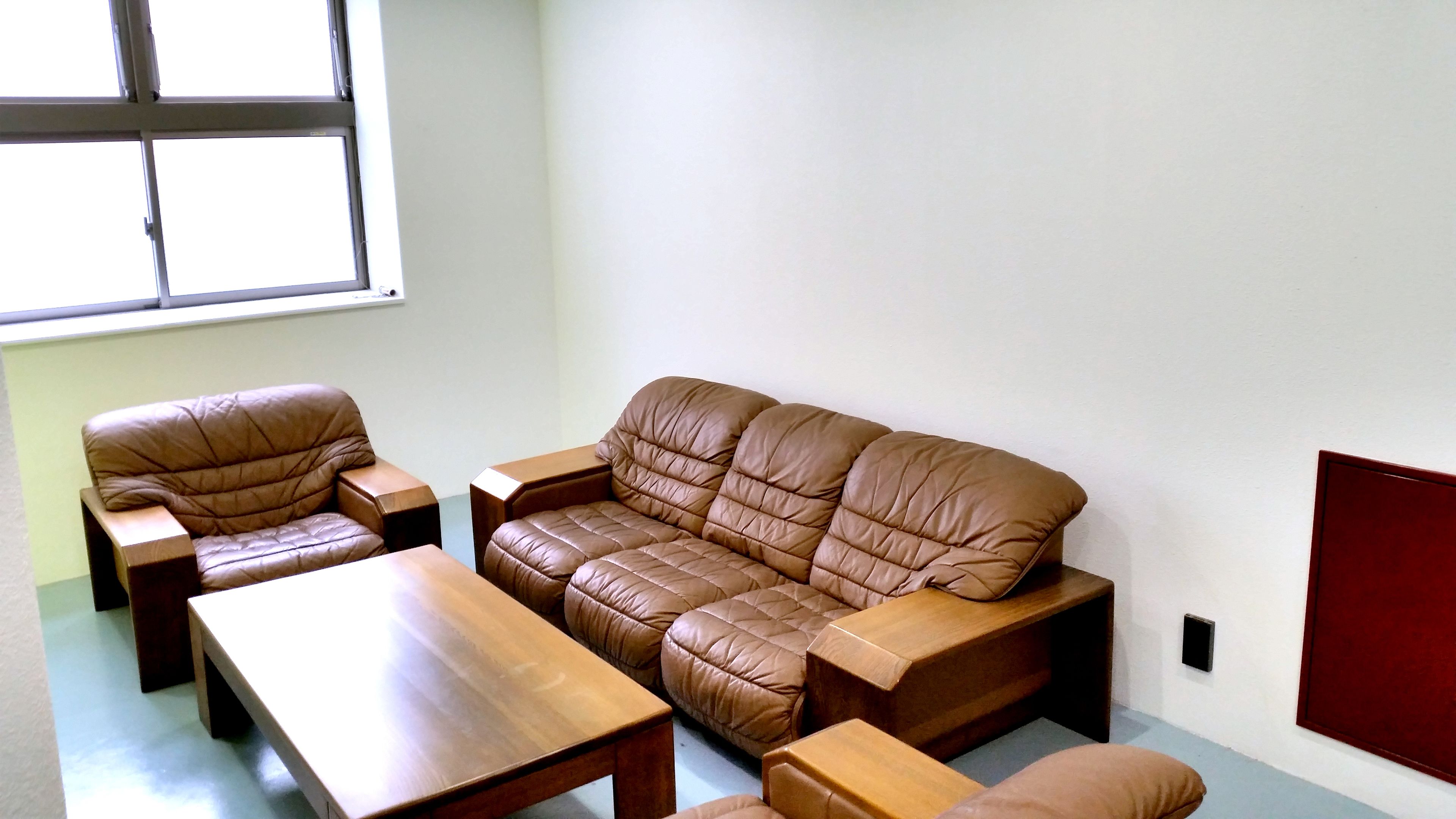 A living room with a brown leather sofa, two armchairs, a wooden coffee table, and a wooden side table.