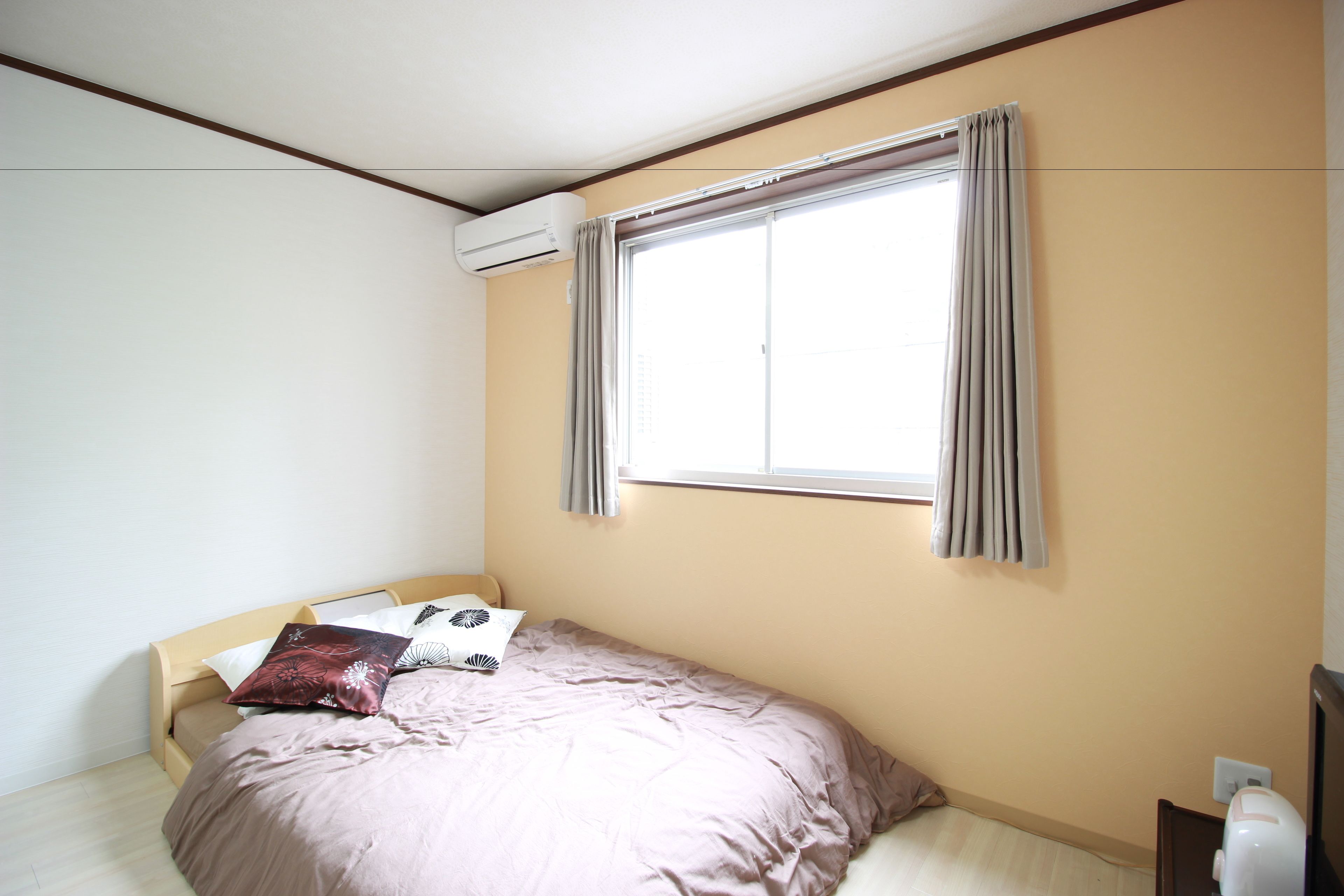 Een slaapkamer met een bed, een raam met gordijnen, een wandairconditioner en een nachtkastje.