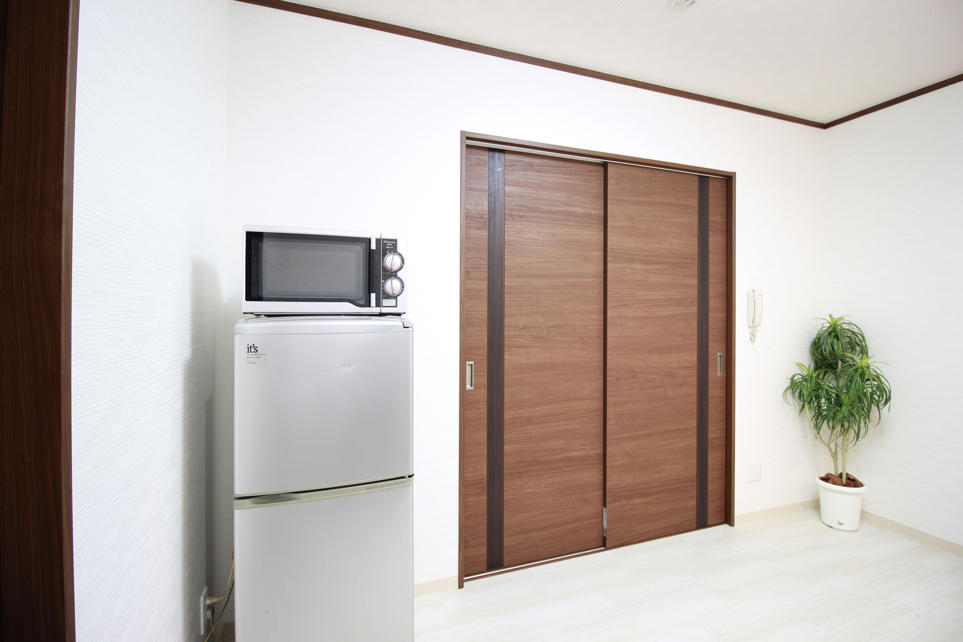 Ein Zimmer mit einem weißen Kühlschrank, einer Mikrowelle und einer Holztür, die sich öffnen lässt.