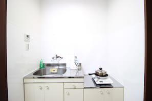 Una pequeña cocina americana con un lavamanos de acero inoxidable, una cafetera, un hervidor y una balanza.