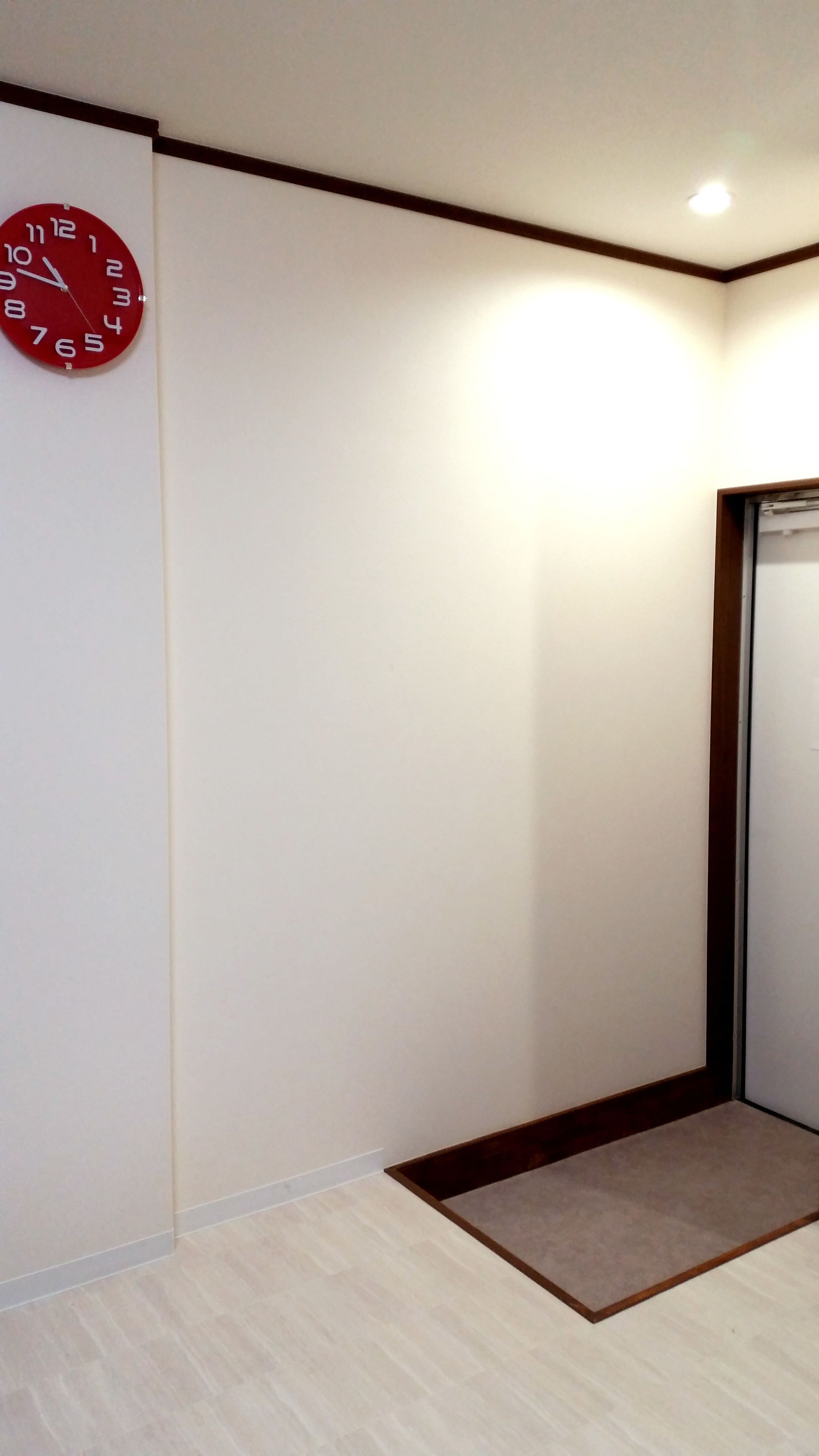 A hallway with a red clock on the wall, a wooden door frame, and a light fixture on the ceiling.