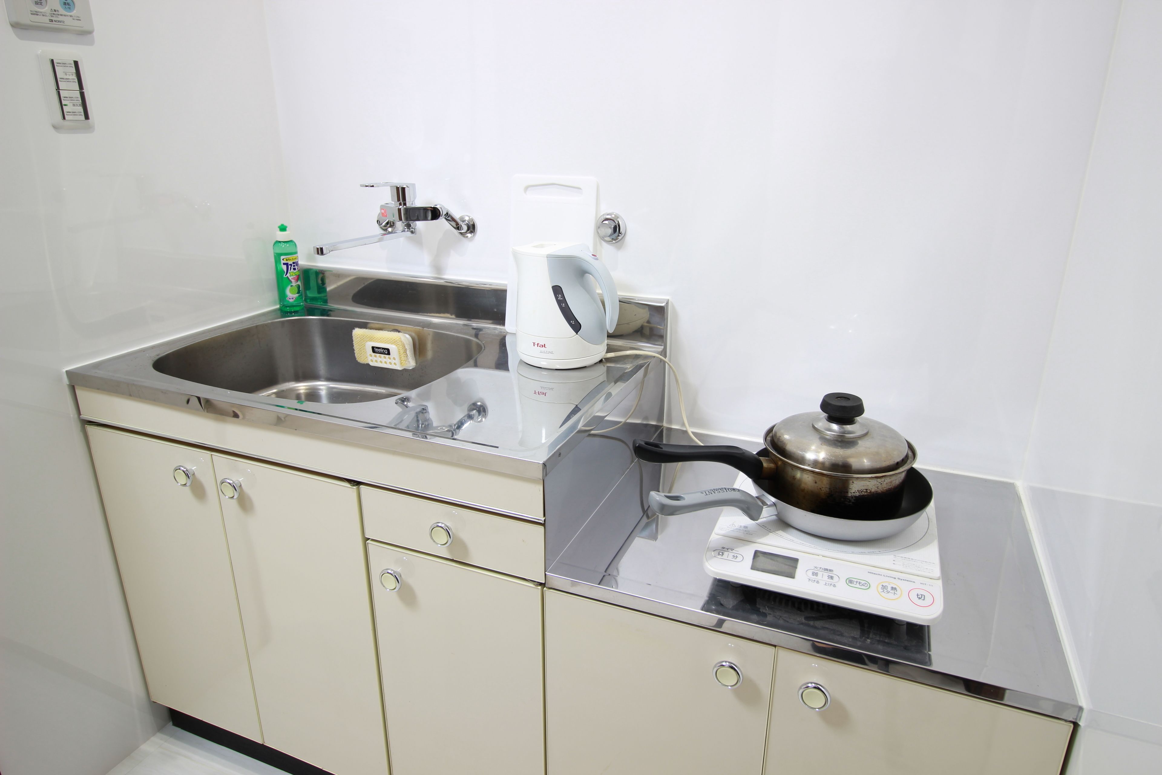 A kitchen with a stainless steel sink, a kettle, a scale, and a pot on the counter.