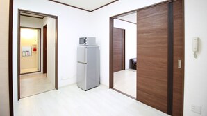 A hotel room with a wooden wardrobe, a small refrigerator, and a telephone. - Mansion Kawata (Osaka)