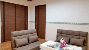 A room with two brown sofas, a glass-top table, and a decorative vase with flowers. - Mansion Kawata (Osaka)