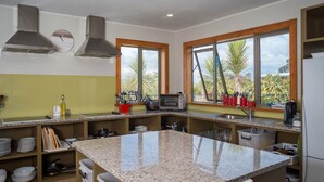 A modern kitchen with granite countertops, a built-in oven, and a large window with a view of palm trees. - Eden's Edge Lodge (Riwaka)