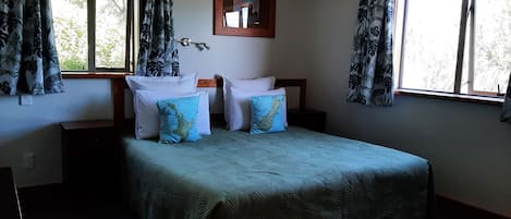 A neatly arranged bedroom with a bed, two nightstands, a mirror, and curtains.