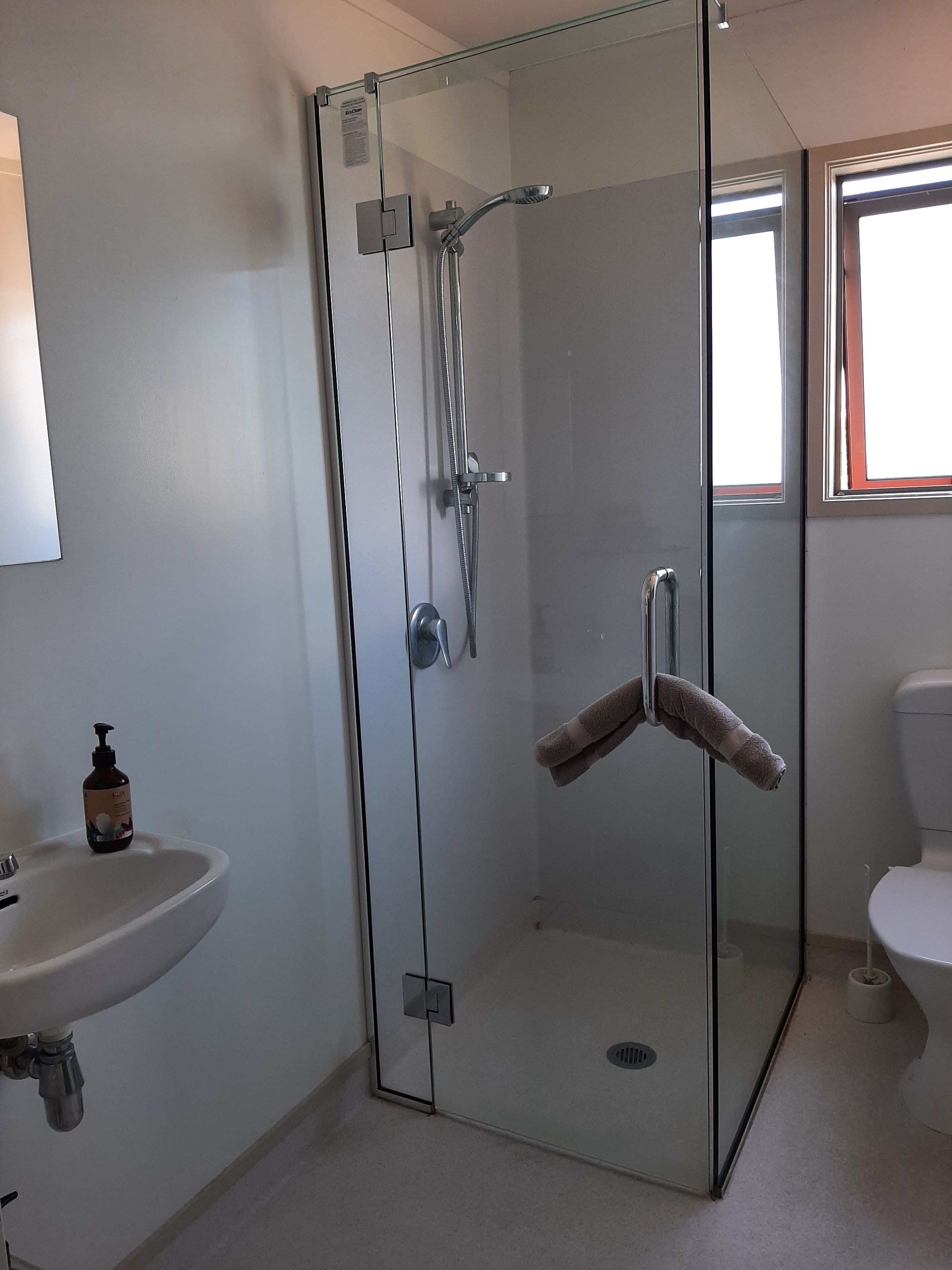 Et moderne badeværelse med en glasafskærmet brusekabine, håndvask og toilet.